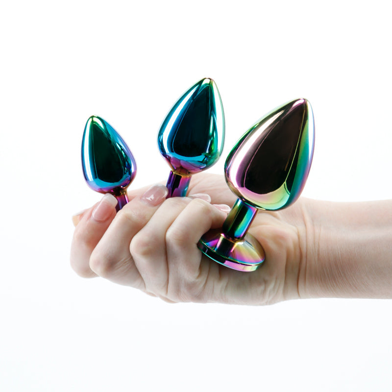 A hand holds three rainbow-colored anal plugs of graduated sizes.