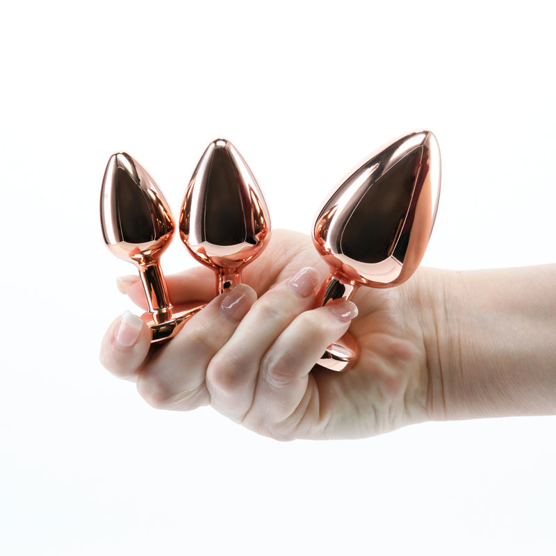 Three rose gold heart-shaped anal plugs held in a hand.