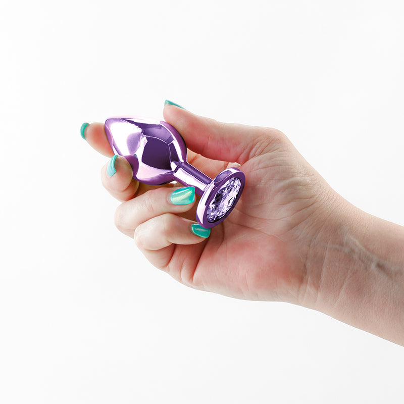 A hand holds a shiny purple anal plug with a crystal accent.