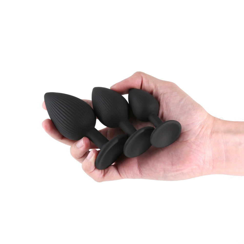 Three black ribbed silicone anal plugs of varying sizes held in a hand.