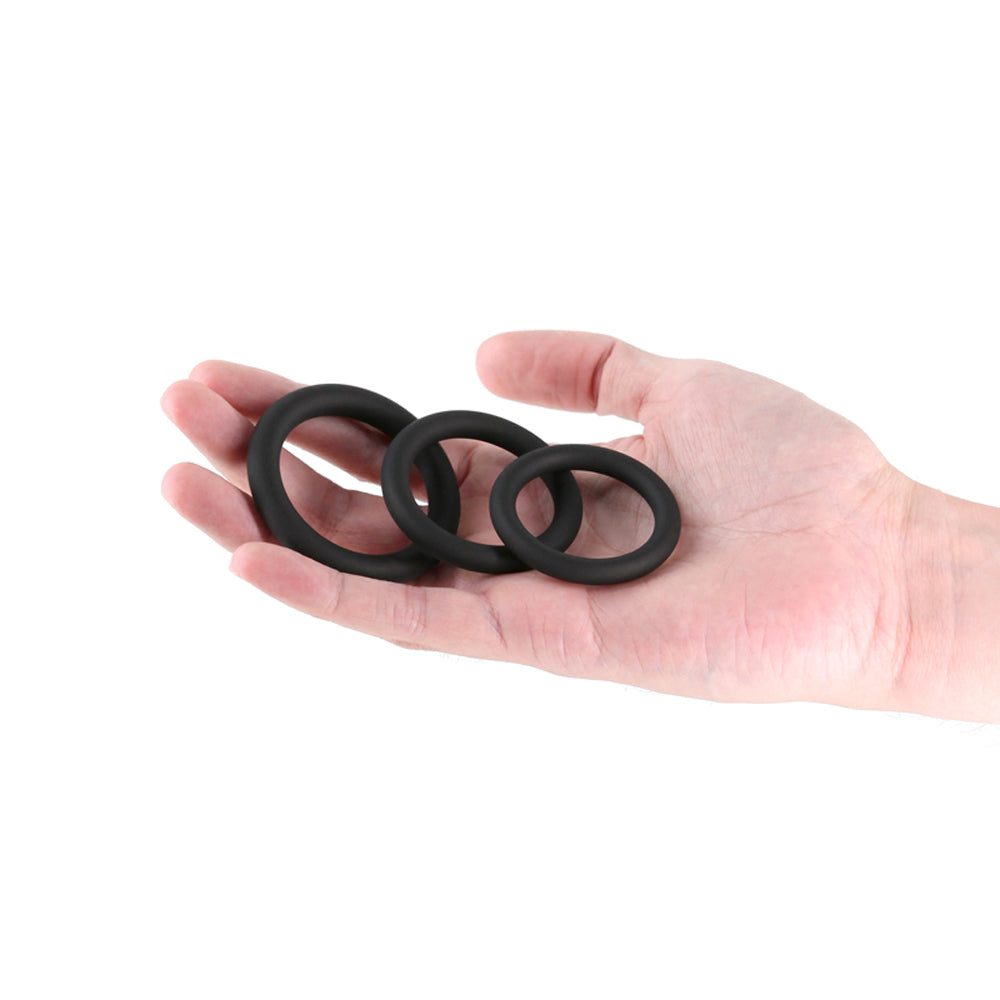 Three black silicone cock rings of varying sizes are held in a hand.