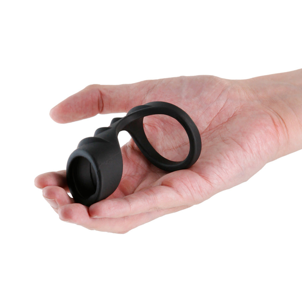 Black silicone penis harness with a ring and textured end held in a hand.