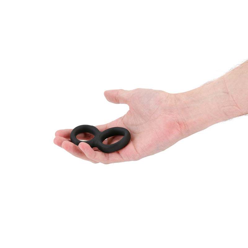 Black stretchy double cock ring held in a hand.