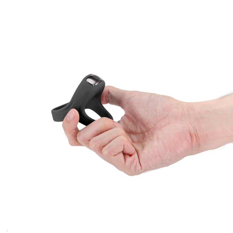 A black vibrating cock ring with a metallic button held in a hand.