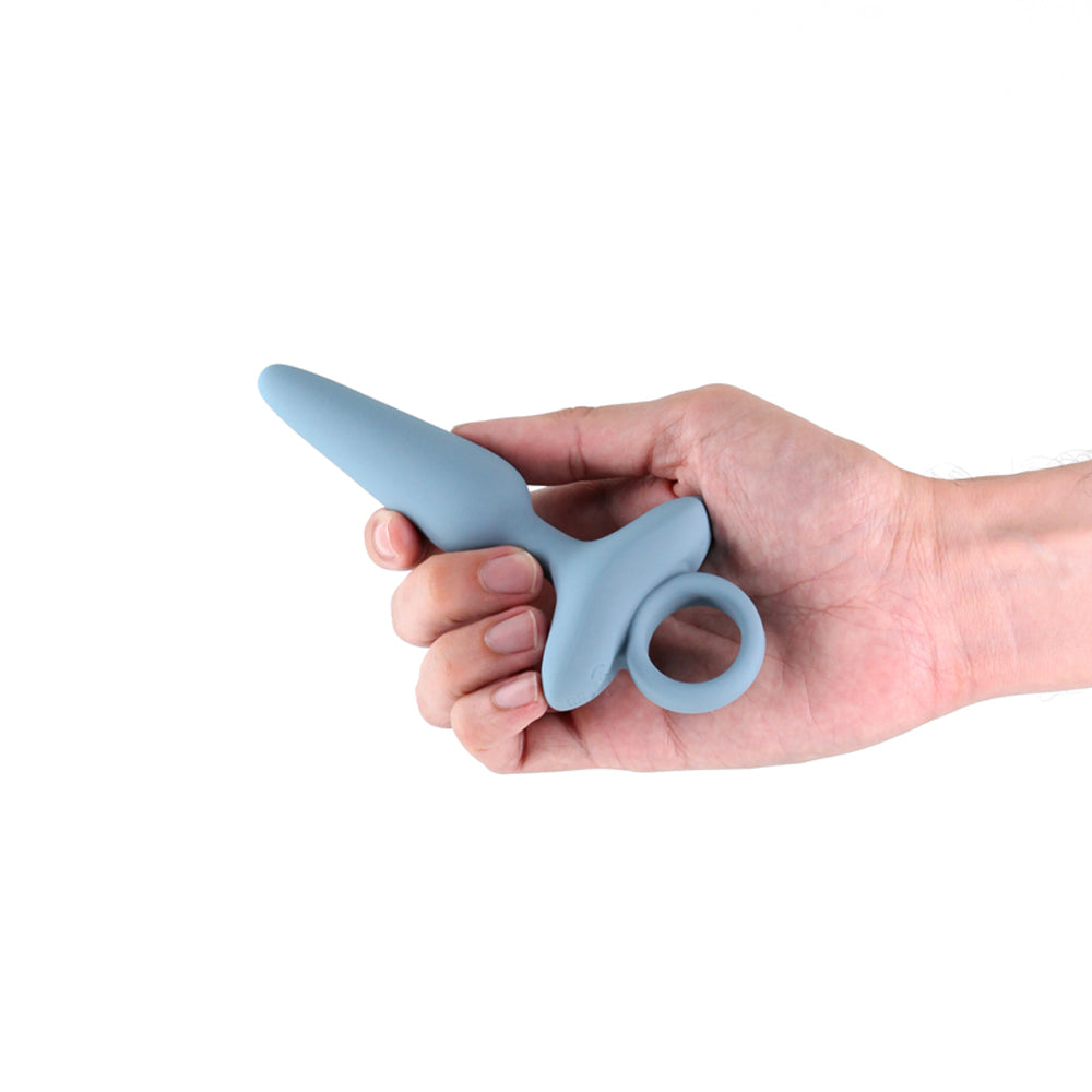 A gray vibrating silicone plug with a ring handle is held in a hand.
