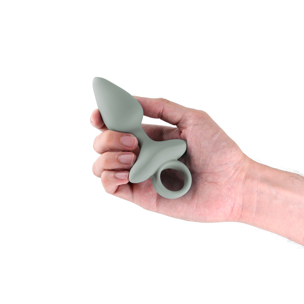 A hand holds a grey silicone anal plug with a ring.