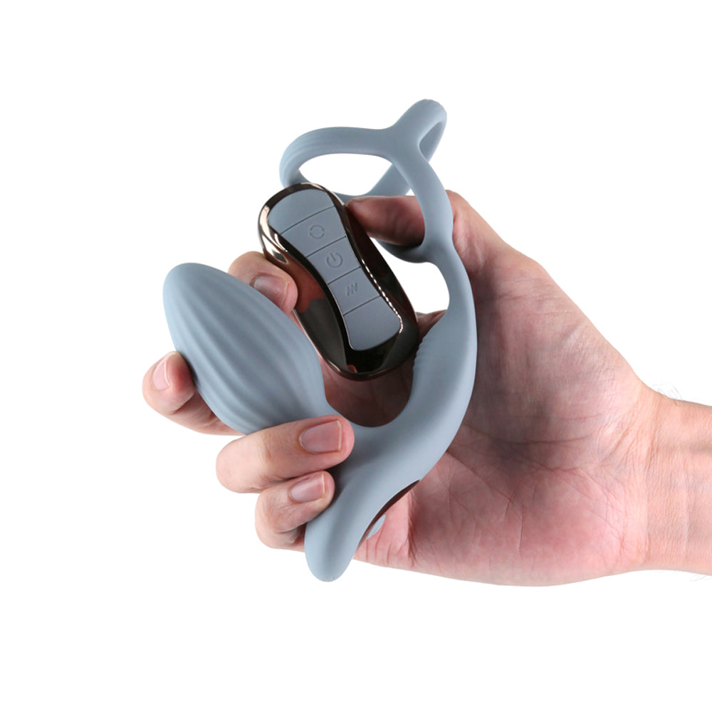 A grey gyrating anal plug with a cock ring and remote control held in a hand.