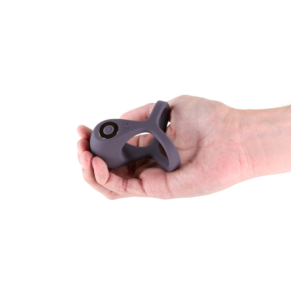 Gray silicone vibrating cock and ball ring held in a hand.