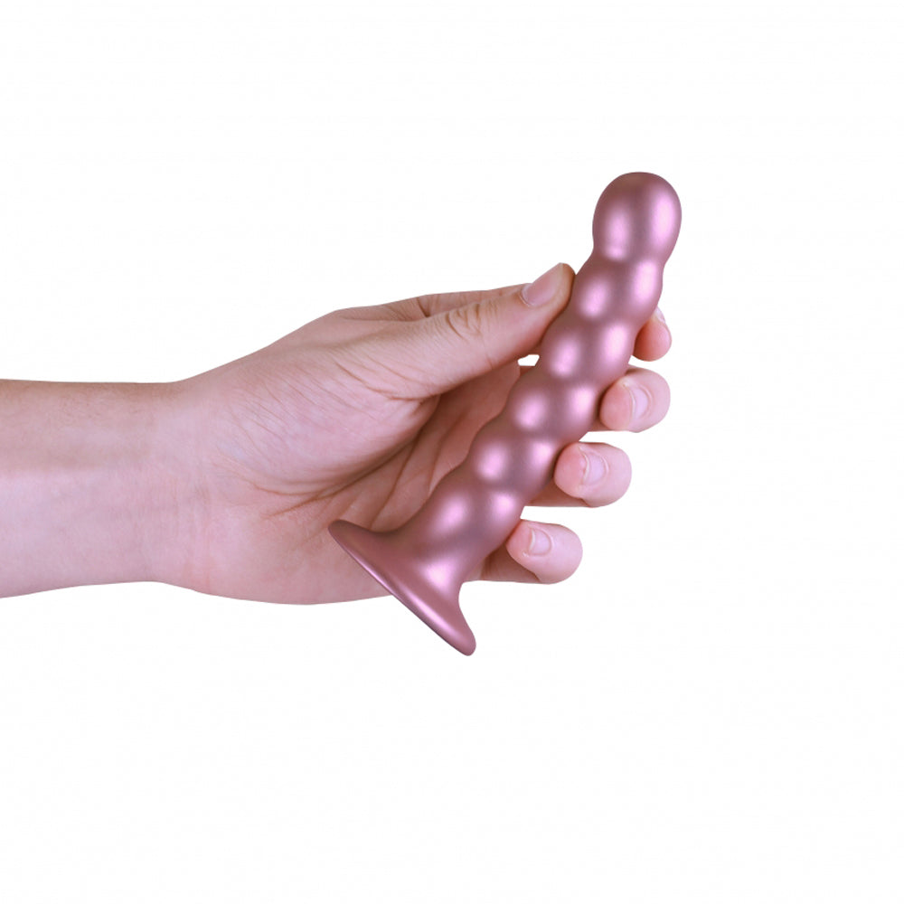 A hand holds a rose gold beaded silicone dildo with a flared base.