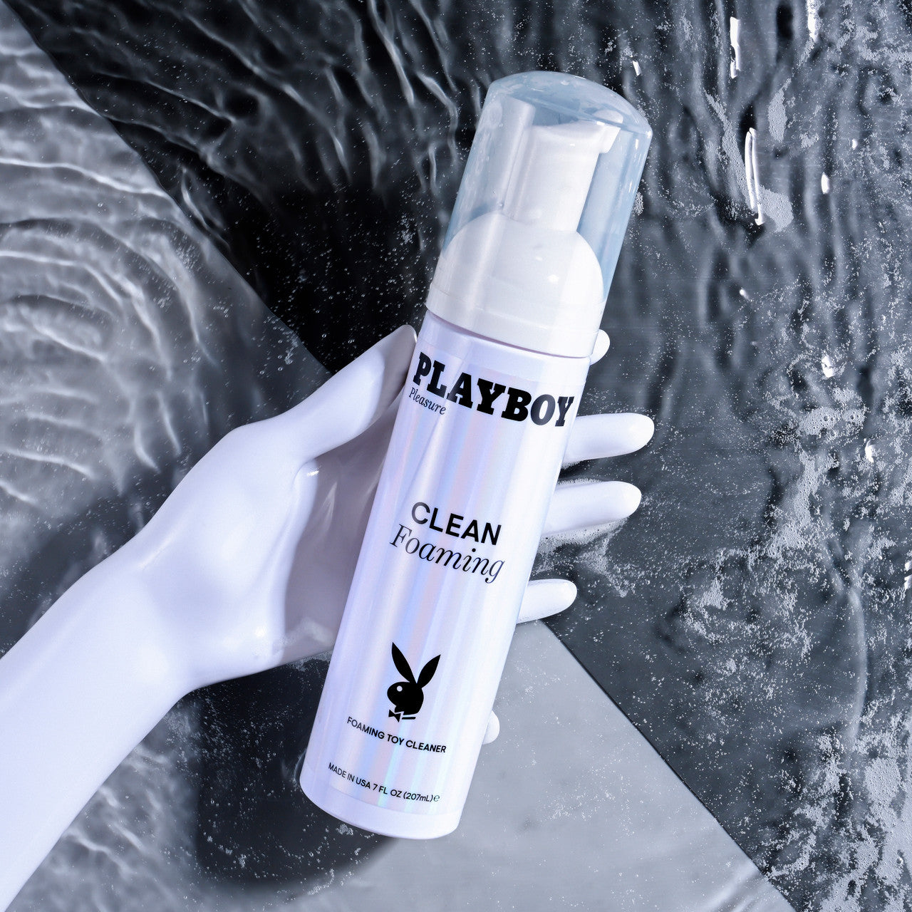 Playboy Clean Foaming Toy Cleanser in a white bottle with a clear cap, held by a white mannequin hand.