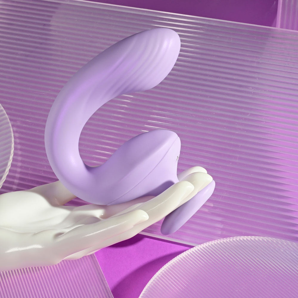 A purple dual motor G-spot vibrator rests on a white hand-shaped stand.