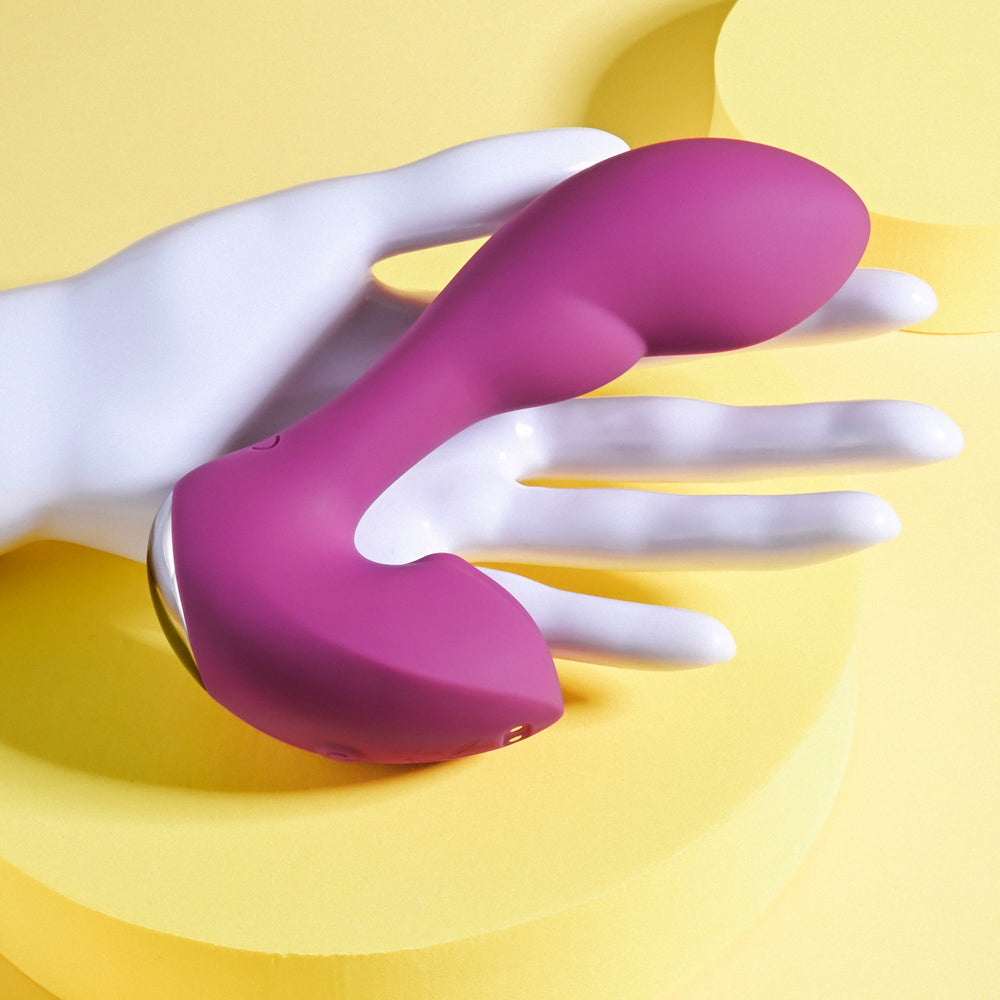 A purple rabbit vibrator with a curved shaft rests on a white mannequin hand.