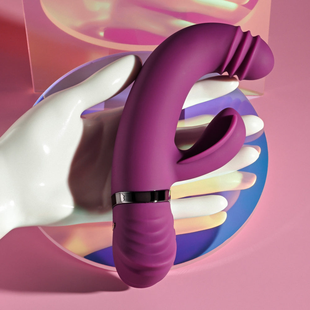 A purple G-spot vibrator with a ribbed tip and a clitoral stimulator rests on a white mannequin hand.