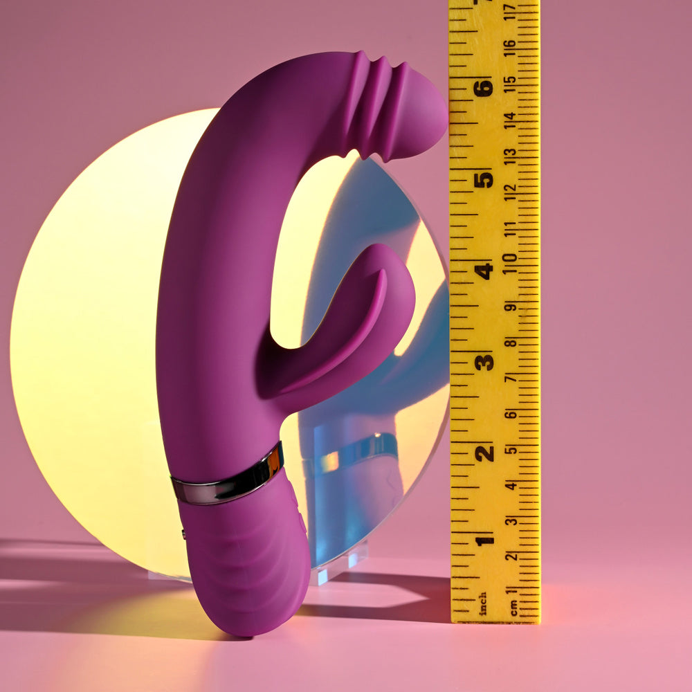 Purple silicone vibrator with a ribbed tip and a clitoral stimulator, next to a ruler.