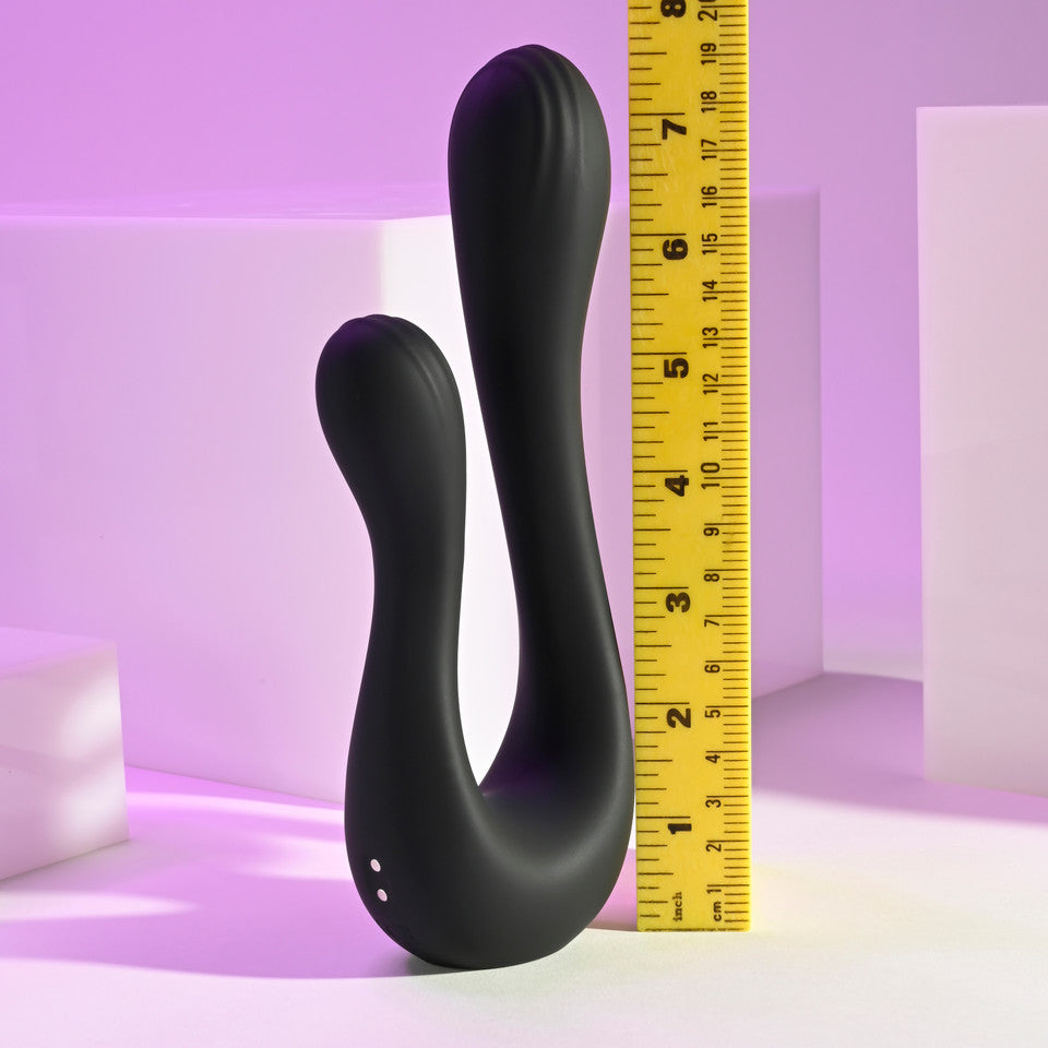 A black dual silicone vibrator with a curved design is shown next to a ruler.