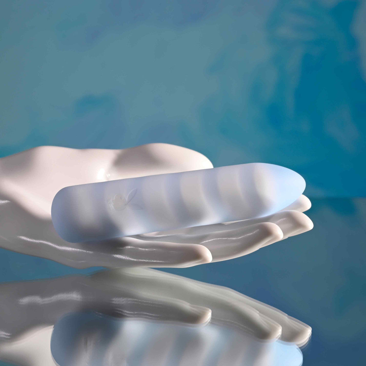 A powder blue silicone bullet vibrator with white swirls rests on a white hand sculpture.
