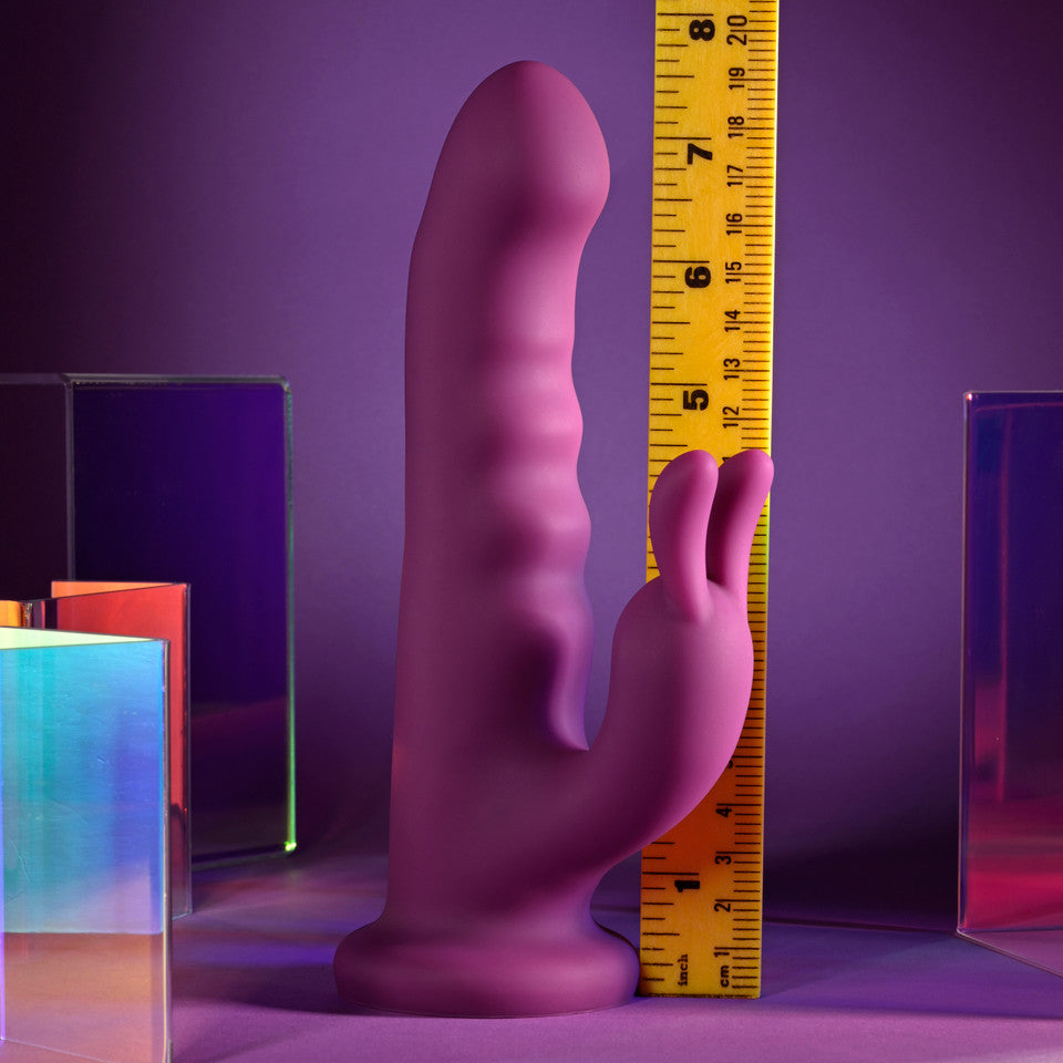 A purple silicone rabbit vibrator with a ruler for scale.