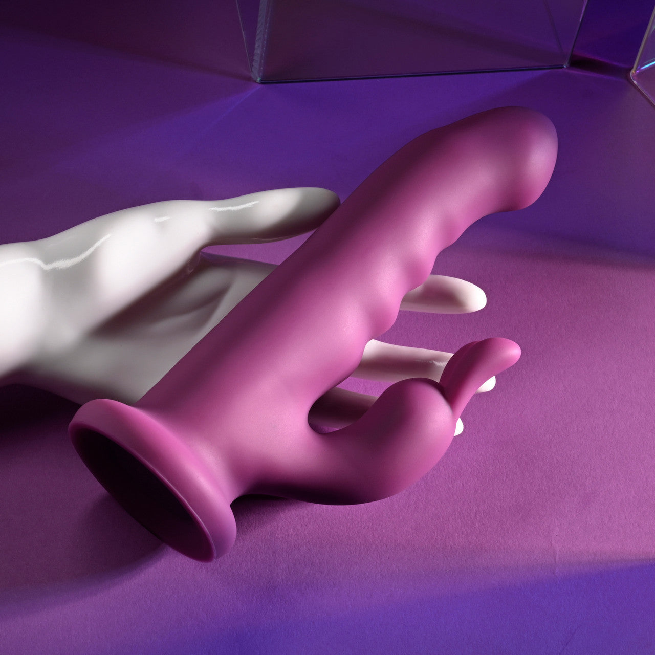 A purple silicone rabbit vibrator with a suction base held by a white mannequin hand.