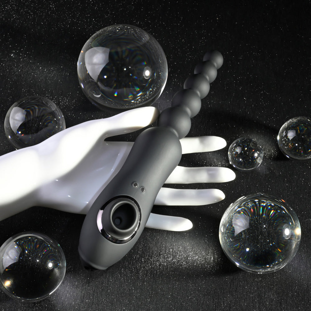 A grey vibrating anal bead toy with clitoral suction rests on a white hand.