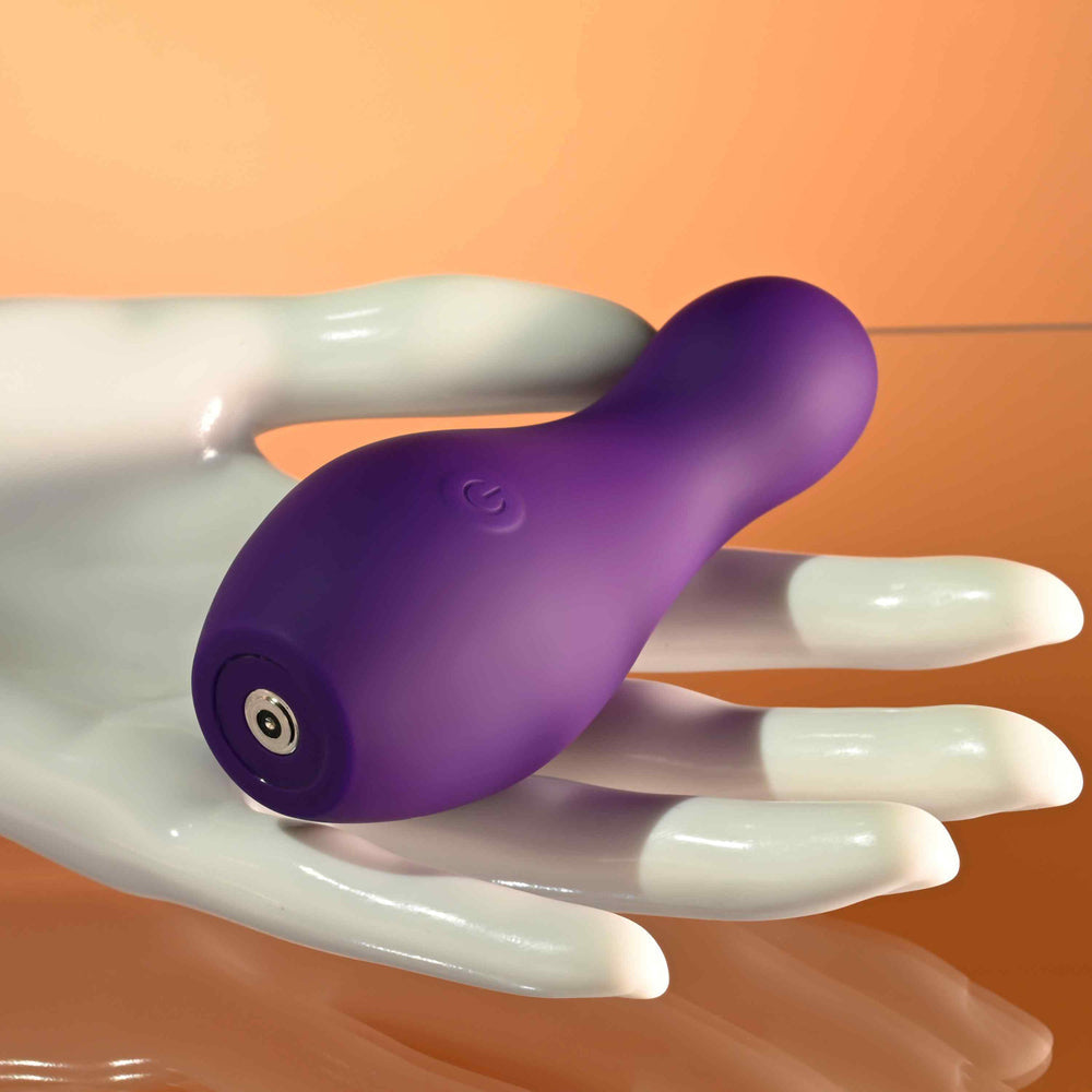 Purple silicone vibrator with a power button symbol rests on a white mannequin hand.