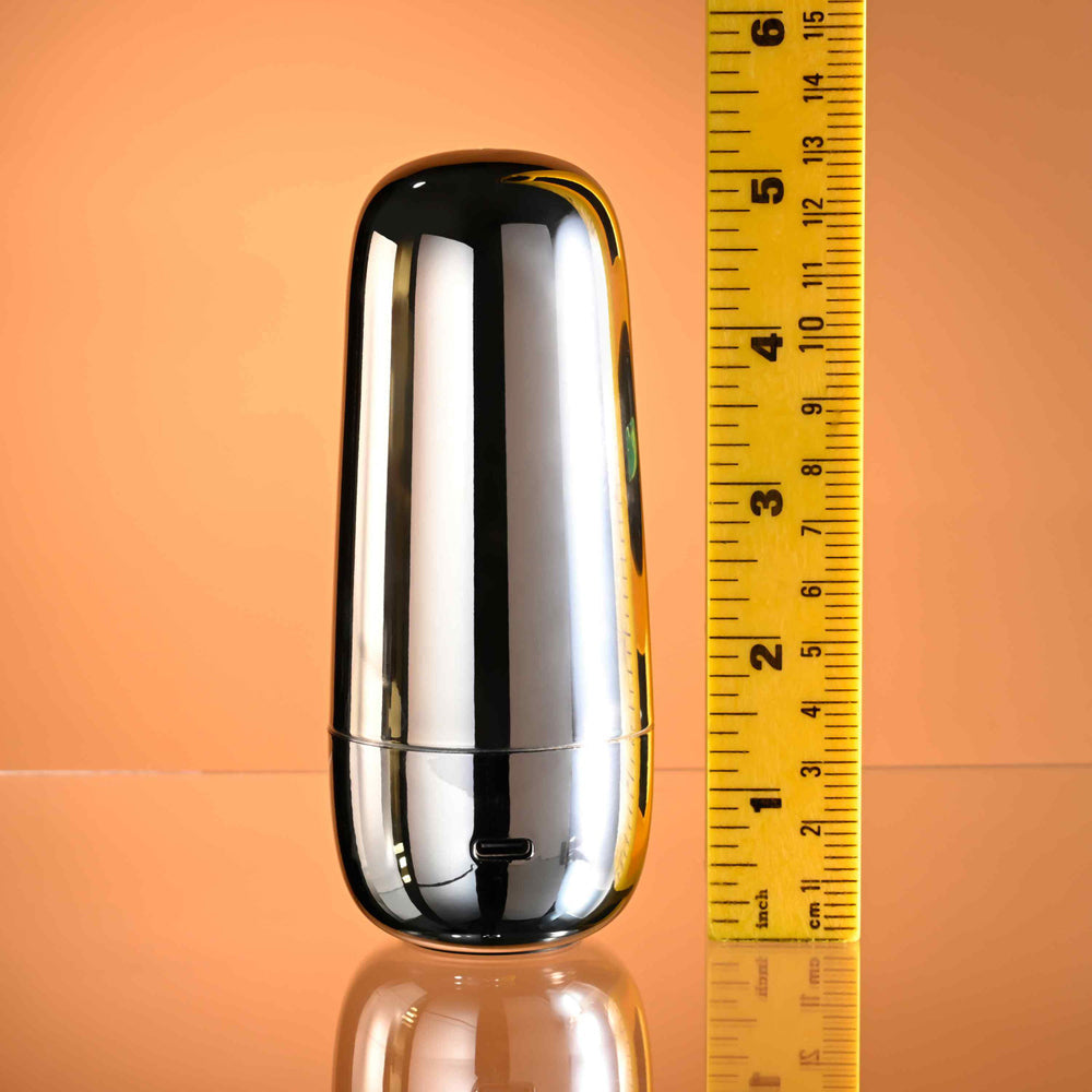 A silver, capsule-shaped vibrator with a USB port, next to a yellow ruler.