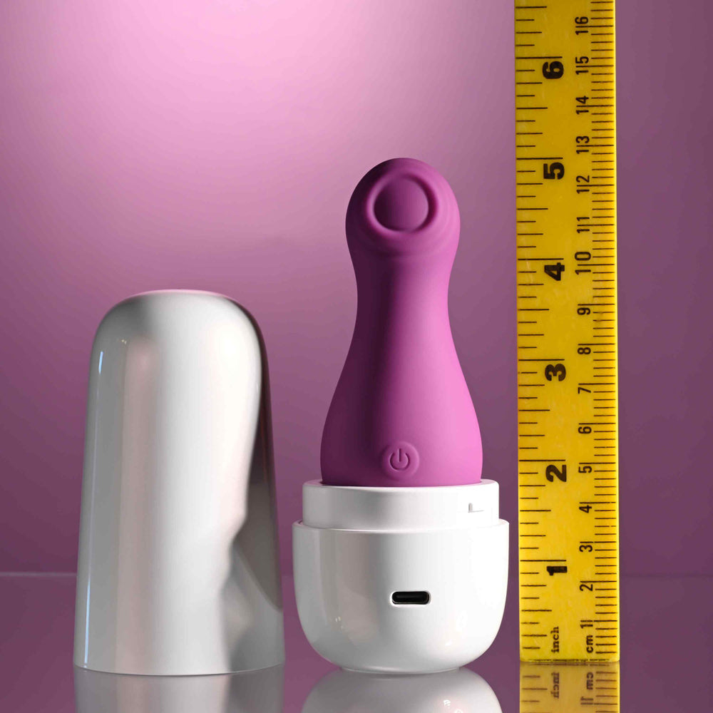 A purple clitoral tapping toy with a white charging case next to a ruler.