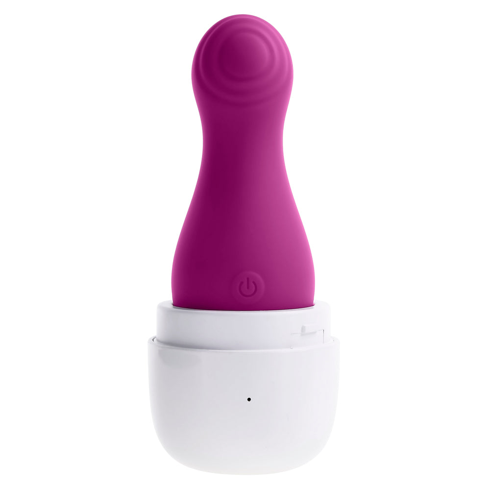 A purple clitoral tapping toy with a power button sits in a white charging case.
