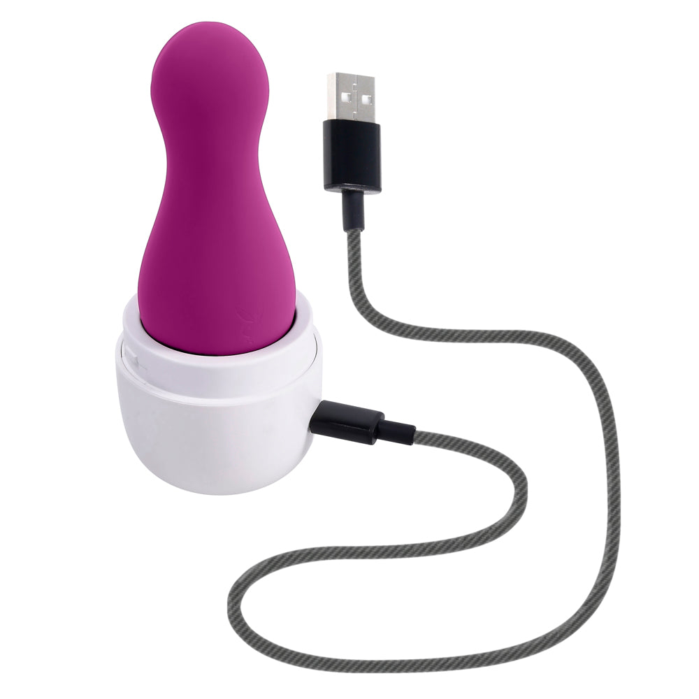 A purple clitoral tapping toy sits in its white charging case with a USB cable.