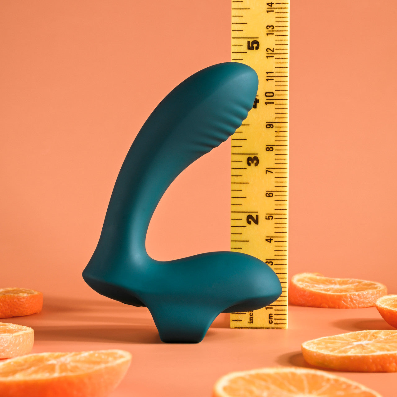 Teal vibrator with finger loop shown next to a ruler and orange slices.
