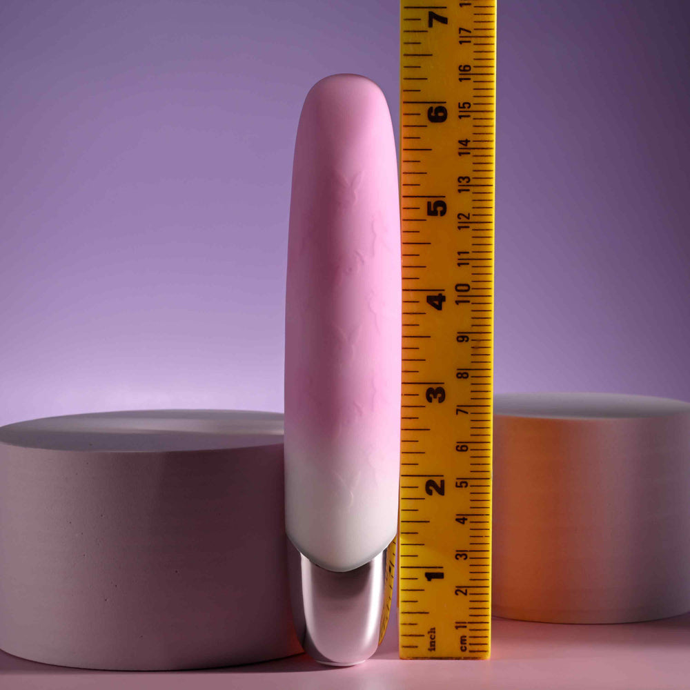 A pink and white gradient bullet vibrator with Playboy bunnies, measured against a ruler.