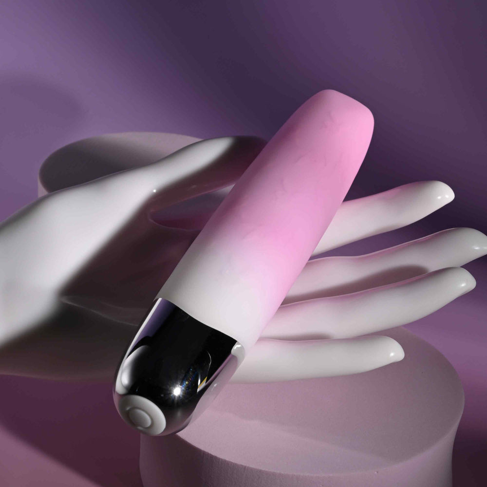 A pink and white gradient bullet vibrator with a silver tip rests on a white hand sculpture.