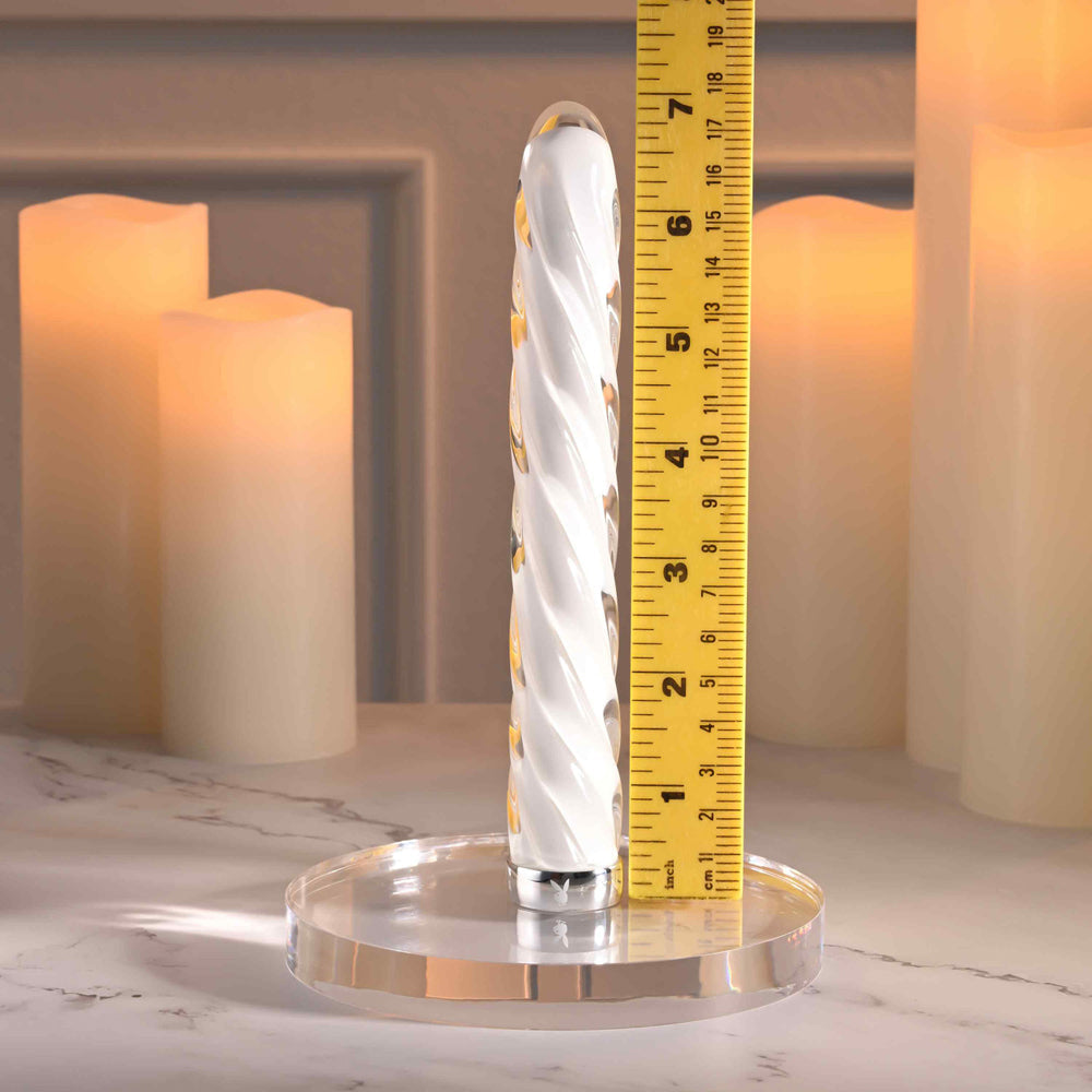 A clear glass vibrator with a spiral design and yellow accents, next to a ruler.