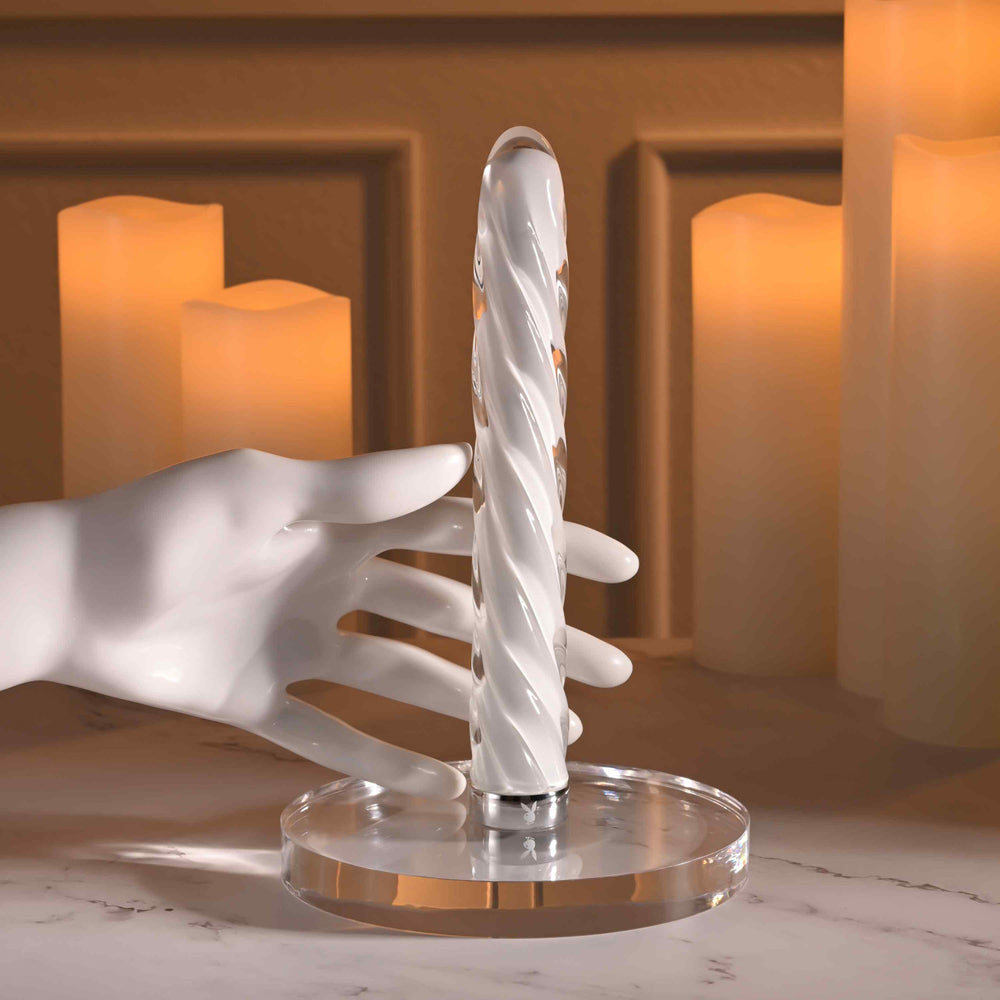A white mannequin hand holds a clear glass vibrator with a spiral design.