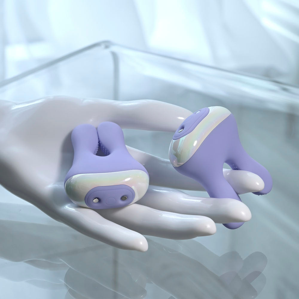 Purple bunny-shaped vibrating nipple clamps with iridescent accents on a white hand.