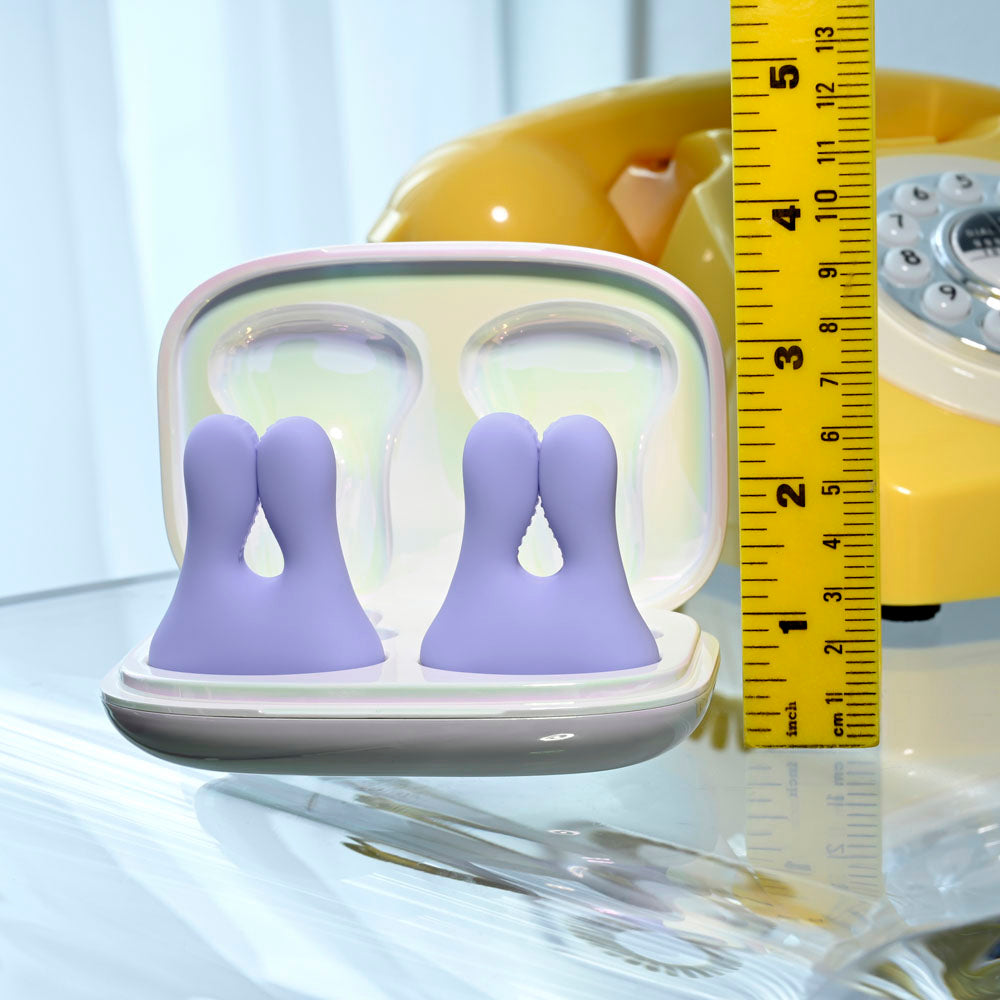Purple vibrating nipple clamps in a charging case next to a ruler.