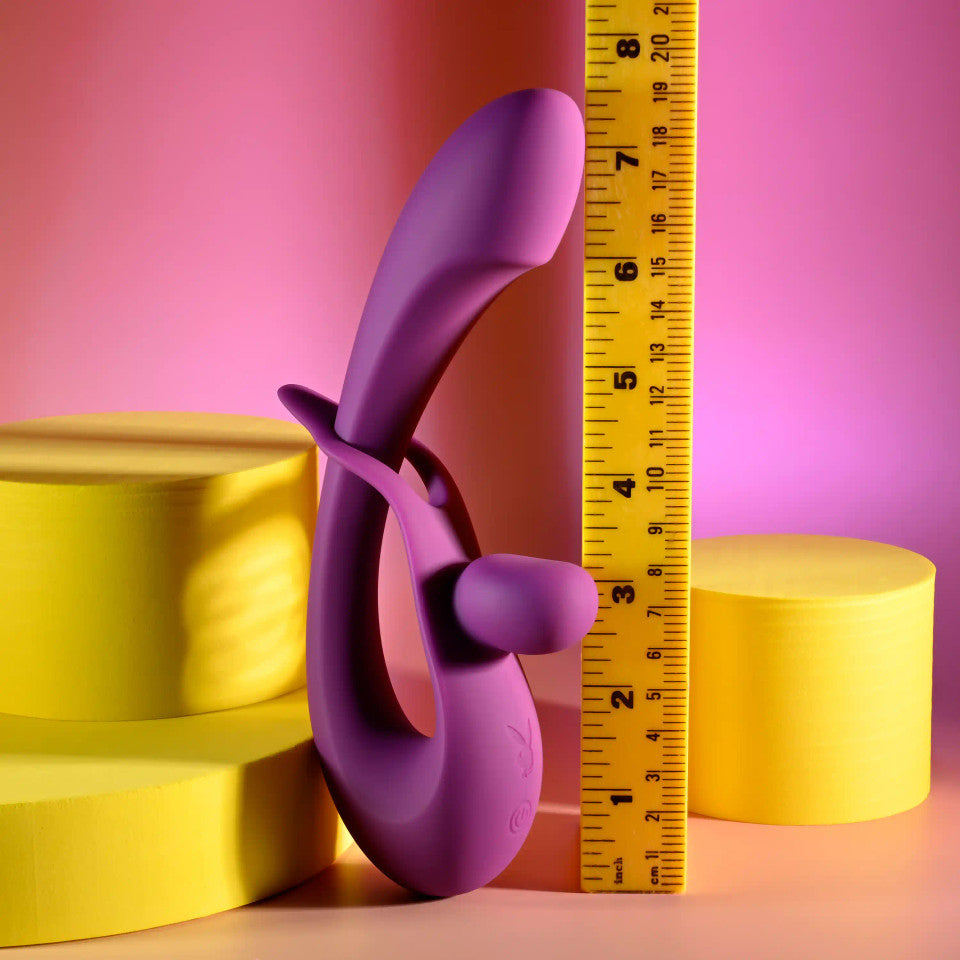 Purple dual silicone vibrator with adjustable shaft next to a ruler.