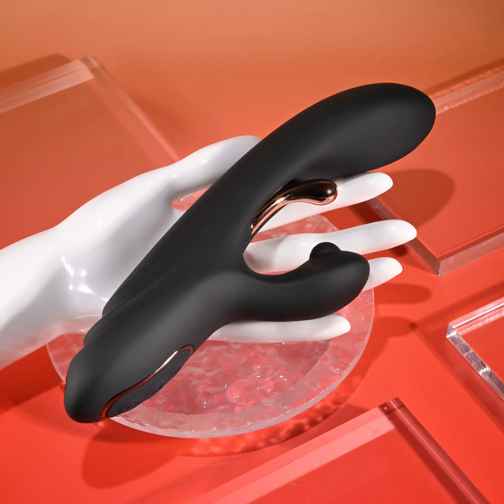 Black silicone dual vibrator with rose gold accents on a white mannequin hand.