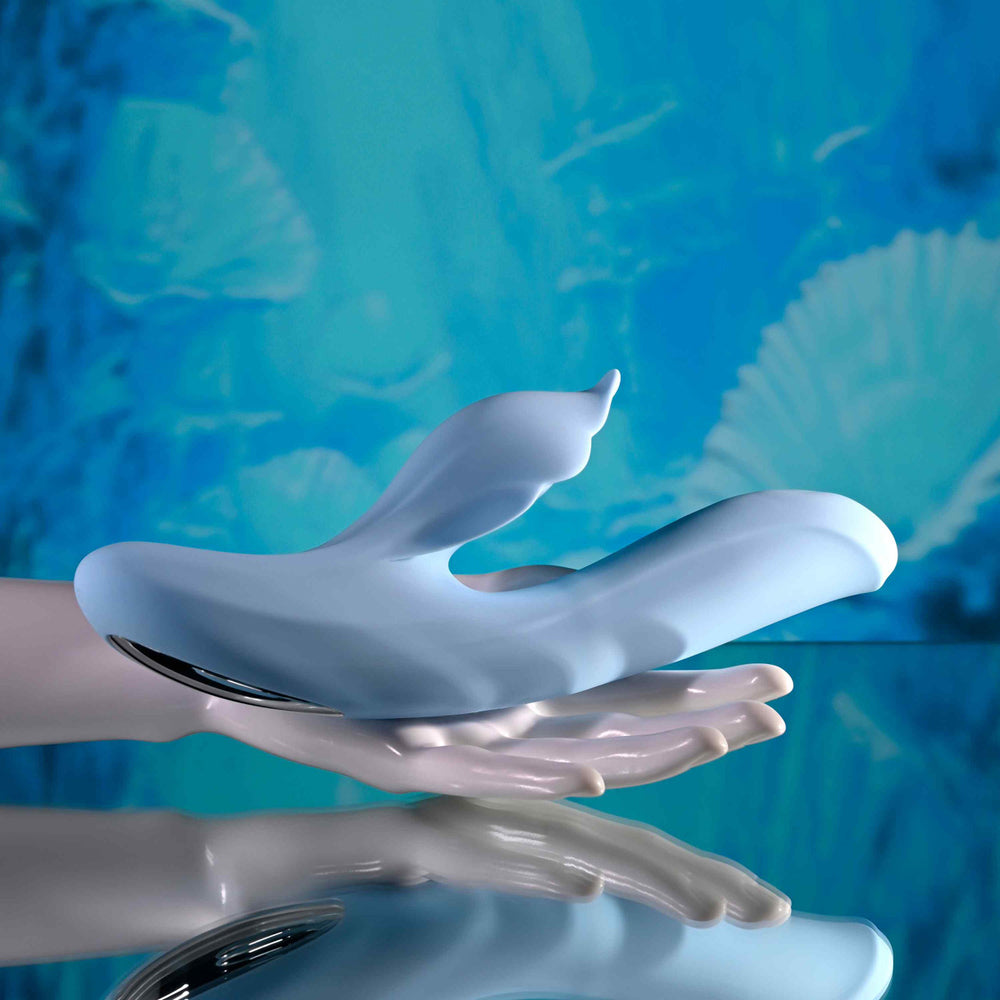 A light blue dual vibrator with a tail-like extension rests on a reflective surface.