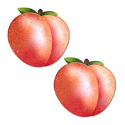 Two sparkling peach-shaped nipple pasties with green leaves.