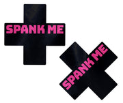 Black cross-shaped nipple pasties with "SPANK ME" in pink lettering.
