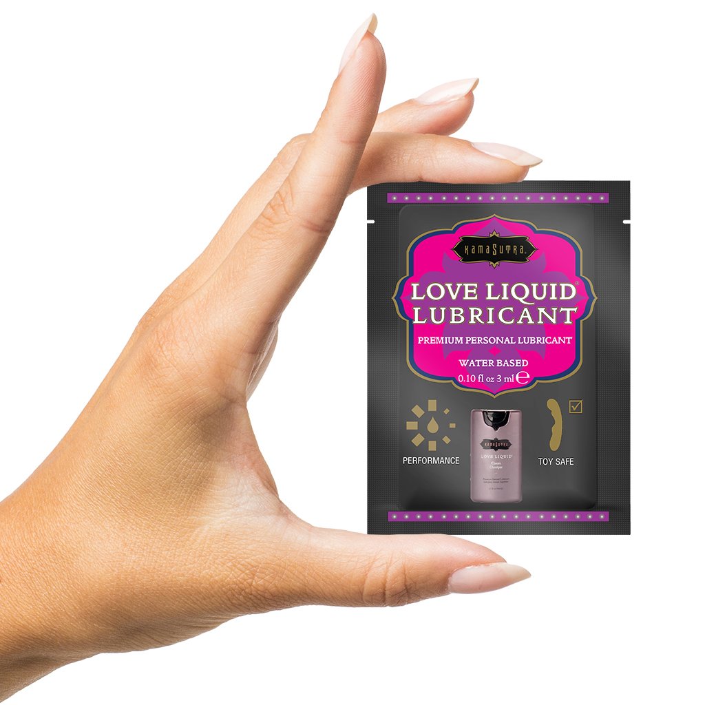 A hand holds a single-use packet of Kama Sutra Love Liquid Lubricant.