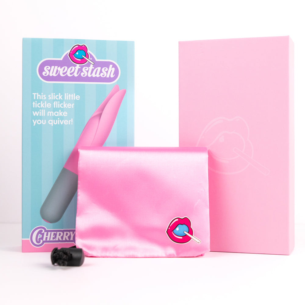 Pink satin pouch with a cherry lollipop design next to a pink box and product packaging.