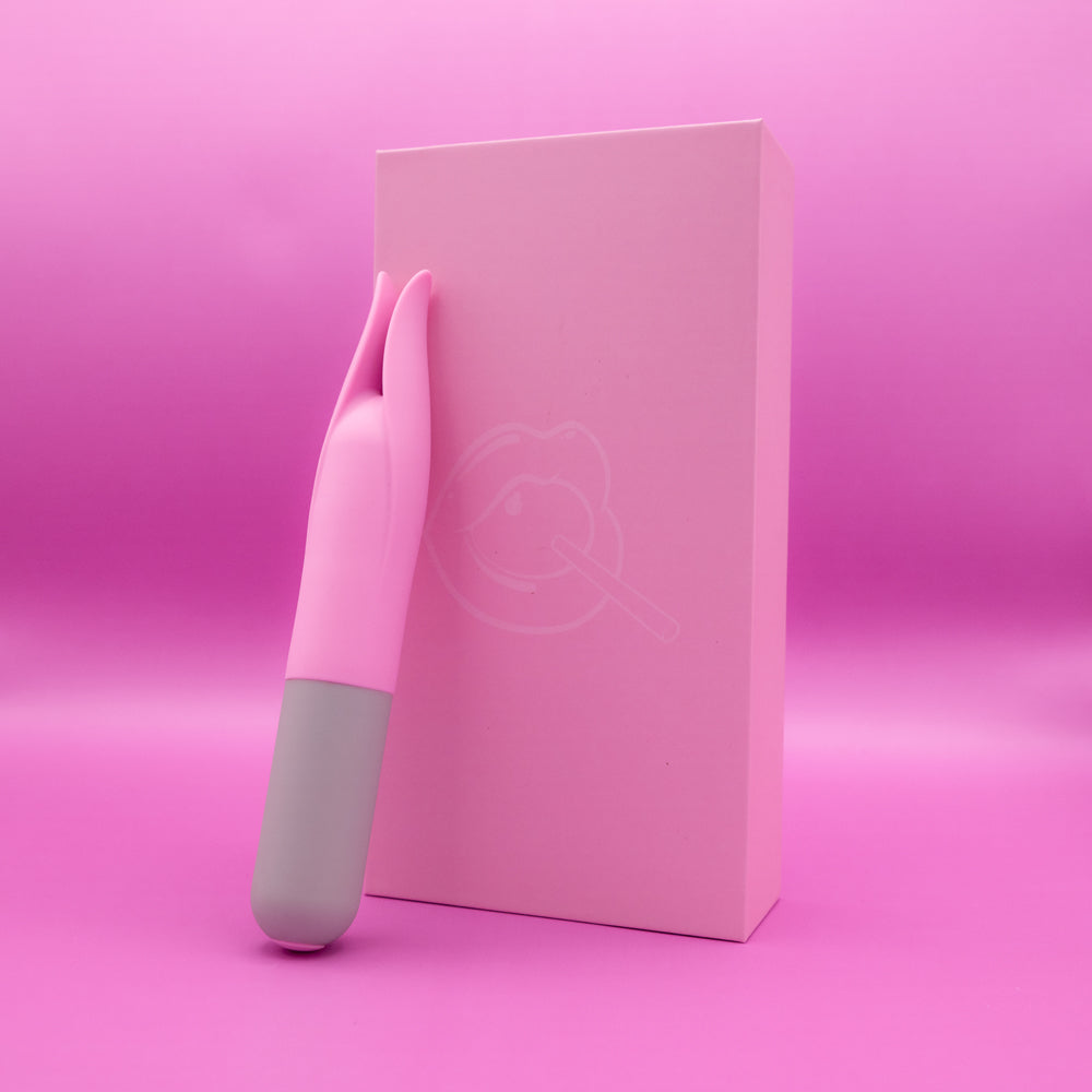 A pink and gray clit tickler rests against a pink box with a lip graphic.