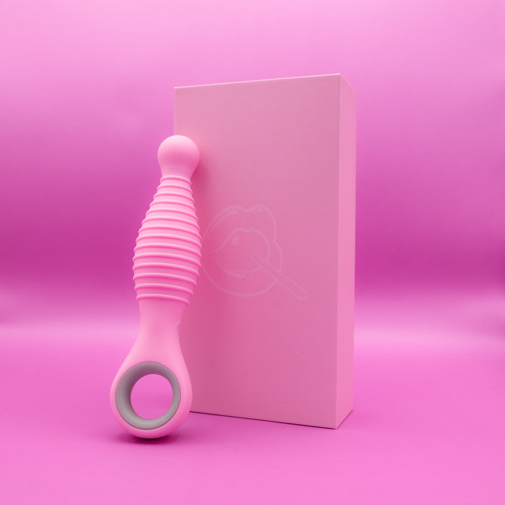A pink ribbed vibrator with a grey ring rests next to a pink box with a lip graphic.
