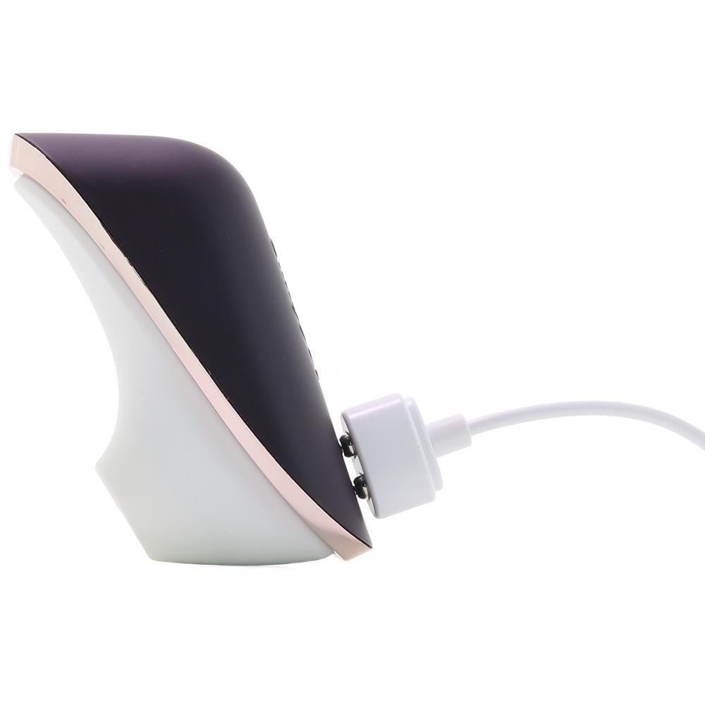 A dark purple and white portable vibrator with a rose gold trim is charging via a white USB cable.