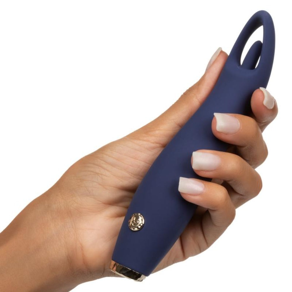 A hand holds a dark blue silicone clitoral massager with a gold button and tip.