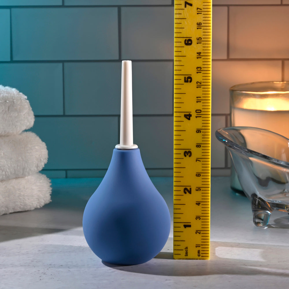 Blue silicone douche with a white tip next to a ruler.