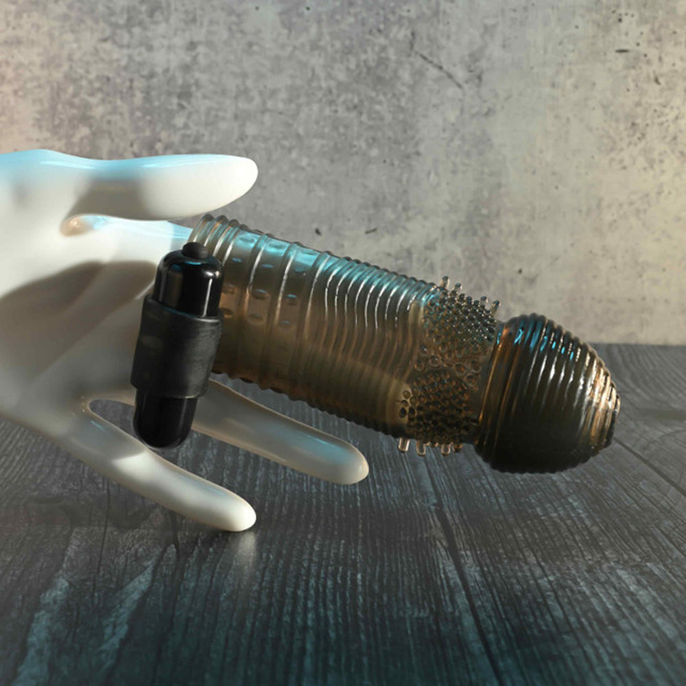 A white hand holds a black vibrating bullet next to a textured, translucent penis sleeve.