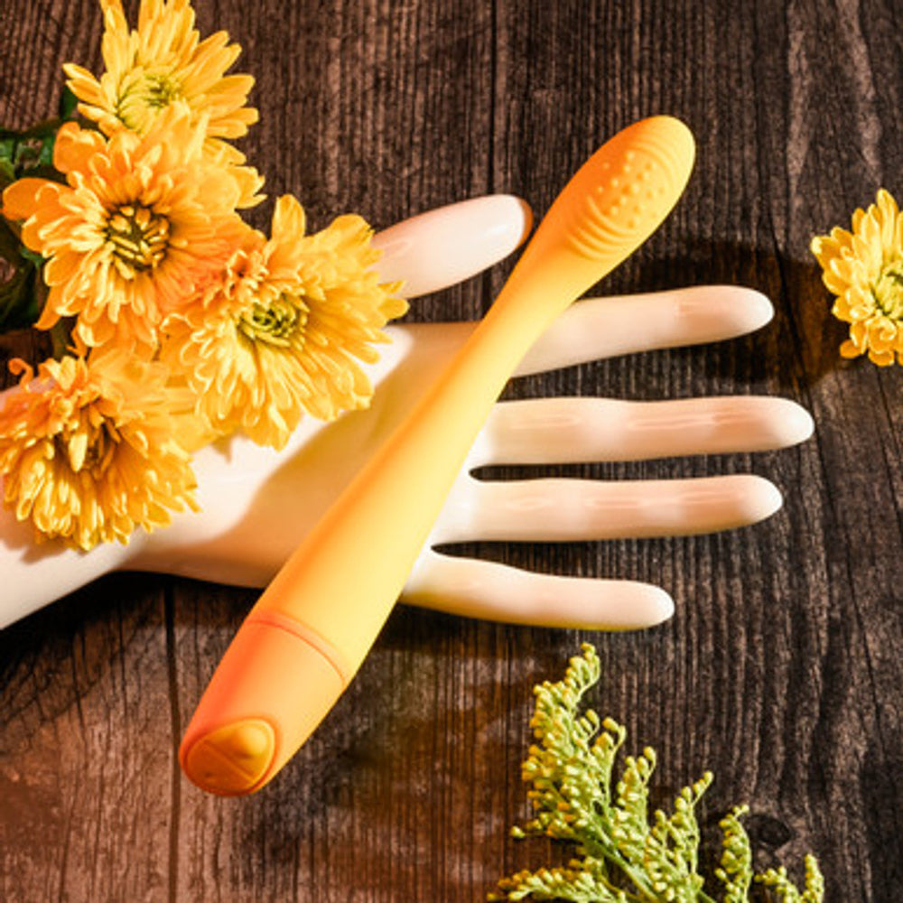 A yellow G-spot vibrator rests on a mannequin hand with yellow flowers.