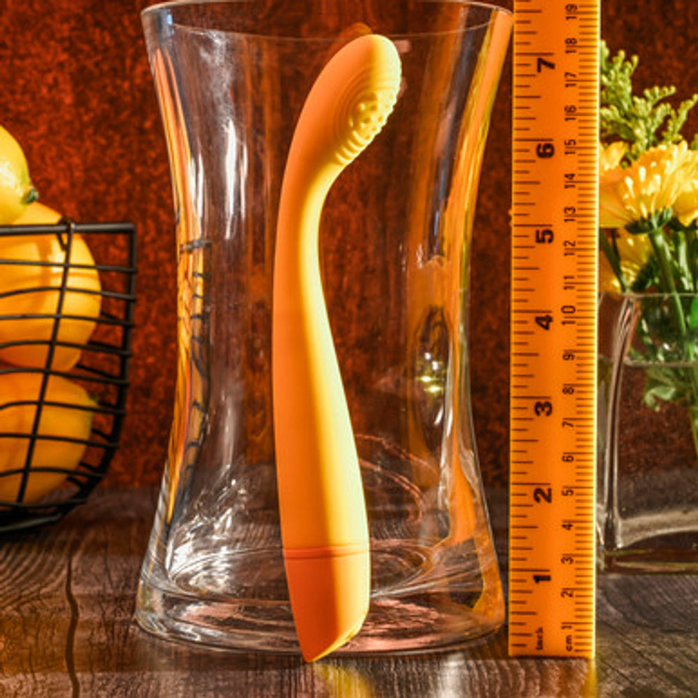 An orange G-spot vibrator with a flexible head is shown next to a glass vase and a ruler.